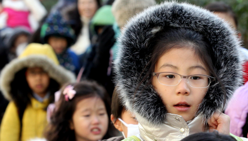 Students of an elementary school in central Seoul huddle against the wind as they go home Friday for a month of winter vacation. (Yonhap News)