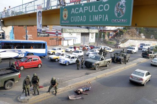 The body of a man that was hanging from a pedestrian bridge prior to the rope slipping loose is guarded by Mexican soldiers in Acapulco, Mexico, Sunday Jan. 9, 2011. Four men were found at the site, two of them decapitated and dismembered. Several separate violent incidents over the weekend in this Pacific resort city have dozens dead. Street sign on bridge reads, 