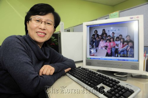 Ahn Shun-hua, founder of Thinking Tree BB Center, poses next to a picture of its Saturday bilingual class at her office in Seoul Women Resource Development Center. (Park Hae-mook / The Korea Herald)