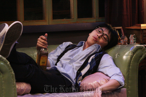 Jo Jeong-seok, one of the main actors of the play “True West,” is slouched on a sofa with a bottle of liquor in hand during a scene. (Aga Company)