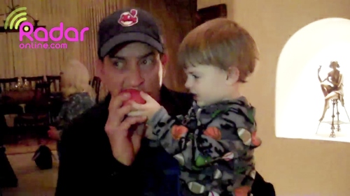 In this image from video released by RadarOnline.com, Charlie Sheen takes a bite from an apple while holding one of his 23-month-old twins before they were removed from his Hollywood Hills home late Tuesday. (AP-Yonhap News)