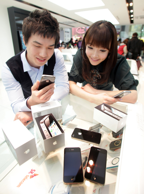 Models look at Apple Inc.’s iPhone 4 at SK Telecom’s T World store in Seoul on Sunday. (SK Telecom)