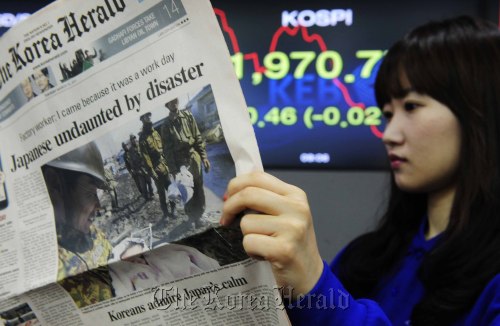 A Korea Exchange official reads The Korea Herald on Tuesday as the stock prices fluctuated in the wake of the Japanese disaster. (Park Hae-mook/The Korea Herald)