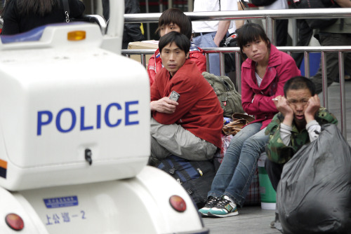 Migrant workers sit near a police electric car patrolling around Shanghai train station on Sunday, May 22, 2011 in Shanghai, China.(AP-Yonhap News)