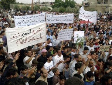 Syrian anti-regime protesters carry banners during a rally in Talbiseh, in the central province of Homs, Syria, on Friday. (AP-Yonhap News)