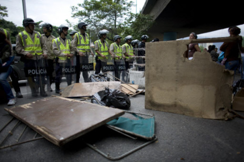 Bolivarian National Police officers stand guard next to a barricade set up by inmates' relatives at a highway in Caracas, Venezuela on May 21 after inmates at the La Planta prison held the warden and 14 other officers hostage.(AP-Yonhap News)