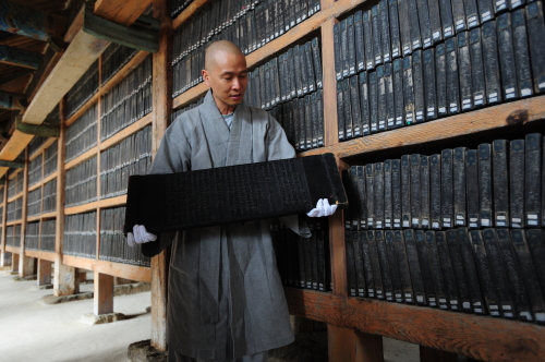 Seong-an, a monk at Haein Temple, shows a wooden block of the Tripitaka Koreana inside the Janggyeong Panjeon at the temple in Hapcheon, South Gyeongsang Province, Thursday. (KBS)