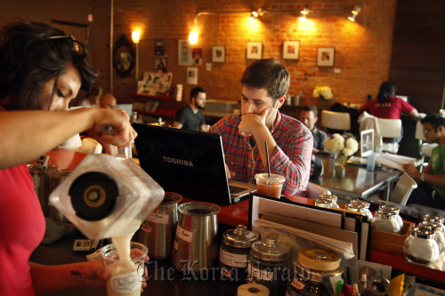 While listening to iTunes, Clay Wheeler (center) uses his laptop to catch up with theatre company work at The Pearl Cup, in Dallas, Texas. (Dallas Morning News/MCT)