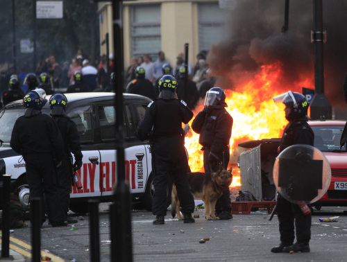 British police officers stand around as a car, background, burns after it was set on fire by rioters in Hackney, east London, Monday Aug. 8, 2011. (AP-Yonhap News)