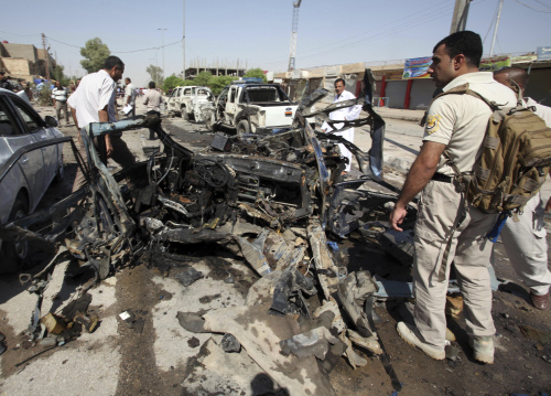 Iraqi security forces inspect the remains of a car used in suicide attack outside a police building on Monday. (AP-Yonhap News)