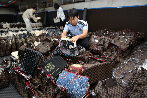 A customs official in Seoul inspects counterfeit designer goods the agency confiscated on Wednesday. (Yonhap News)