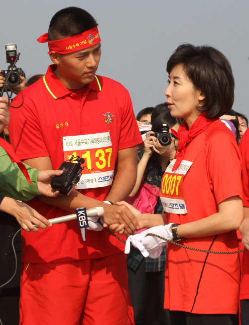 Rep. Na Kyung-won of the Grand National Party (right) shakes hands with Hyun Bin, a former actor currently serving his military service in the Marines, during a marathon event in Yeouido, Seoul on Sunday. (Yonhap News)