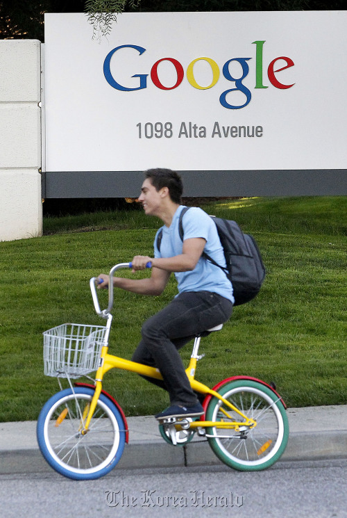 A Google Inc. employee rides a “G-bike” past signage displayed company headquarters in Mountain View, California. (Bloomberg)