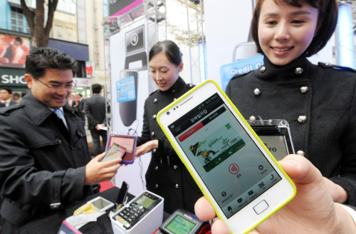 A citizen taps a cell phone on a NFC chip reader during a mobile payment event held in Myeong-dong, central Seoul. (Ahn Hoon/The Korea Herald)