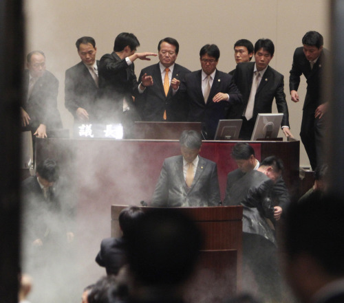 Rep. Kim Sun-dong (center at the podium) of the Democratic Labor Party stands in silent protest after detonating a tear gas grenade and dousing himself with the powder to block the approval of the free trade agreement with the U.S. in the National Assembly on Tuesday (Park Hyun-ku/The Korea Herald)