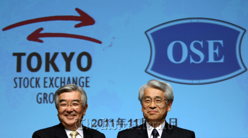 Atsushi Saito, president and chief executive officer of Tokyo Stock Exchange Group Inc. (left), poses with Michio Yoneda, president of Osaka Securities Exchange Co., during a photo session at a news conference in Tokyo on Tuesday. (Bloomberg)