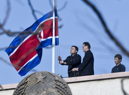North Korean embassy staff members lower their national flag to half-mast to mourn the death of North Korean leader Kim Jong-il on the roof of the embassy in Beijing, China, Monday. (AP-Yonhap News)