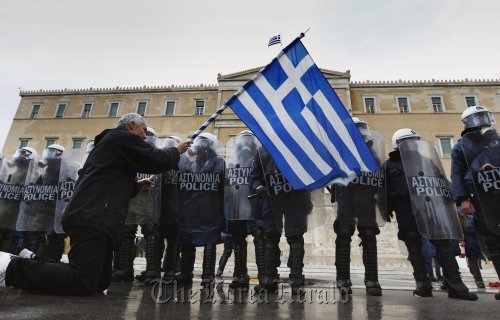 An anti-austerity protester waves a Greek flag in front of the heavily guarded parliament in Athens Feb. 7. (Reuters-Yonhap News)