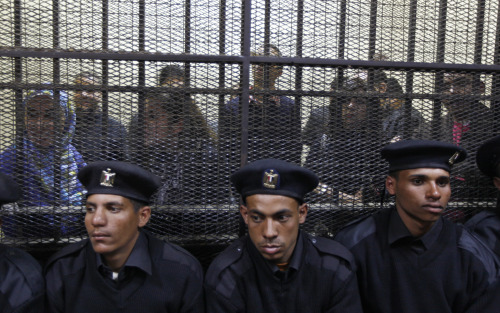 Egyptian policemen sit in front of Egyptian employees of several pro-democracy groups charged with using foreign funds to foment unrest during their trial in Cairo on Sunday. (AP-Yonhap News)