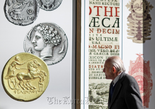 A pedestrian looks at an advertisement displaying Greek coins outside the headquarters ofAlpha Bank AE in Athens. (Bloomberg)