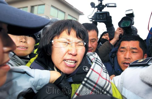 Jeju council member Kim Young-shim of the Unified Progressive Party is taken away by the police after she tried to stop vehicles barricading a bridge near the site of the Jeju naval base from being towed away on Wednesday. The contractors building the base began demolition work to remove rocks and man-made features from the area. (Yonhap News)
