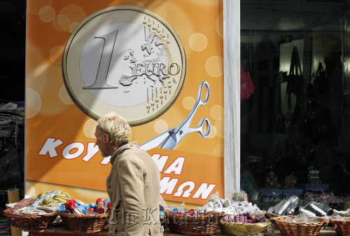 A pedestrian passes a euro coin advertisement which reads “prices haircut” in Athens on Wednesday. (Bloomberg)