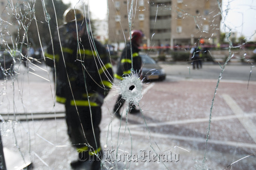 Israeli firefighters are seen through a shattered window after a rocket fired by Palestinian militants from the Gaza Strip hit the city of Ashdod, Israel, Monday. (AP-Yonhap News)