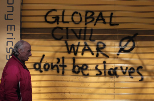 A pedestrian walks by graffiti on a shuttered shop window in Athens on Saturday. (AP-Yonhap News)