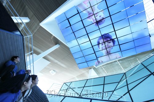 Visitors look at LG’s media chandelier, composed of 54 display panels, which shows dynamic artwork accompanied by sound at its building constructed for the Expo 2012 in Yeosu on Sunday. (LG Group)