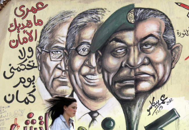 An Egyptian woman walks in front of graffiti with faces of ousted president Hosni Mubarak (right), military ruler Hussein Tantawi (second from right), presidential candidates Amr Moussa (second from left) and Ahmed Shafiq (left) with Arabic that reads, “I will never give you peace and you will not rule me another day,” at Tahrir Square, the focal point of the Egyptian uprising, in Cairo on Tuesday. (AP-Yonhap News)