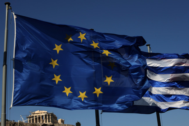 An EU and a Greek flag fly in front of ancient Parthenon temple in Athens on Sunday. ( AP-Yonhap News)