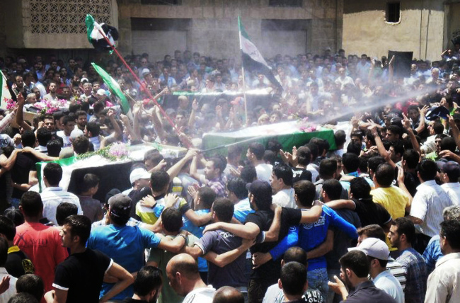 This citizen journalism image provided by Shaam News Network SNN, purports to show an anti-Syrian regime man (center), spraying water over mourners to cool them from the heat as they carry the coffins of those killed by the Syrian forces shelling in Daraa on Tuesday. (AP-Yonhap News)