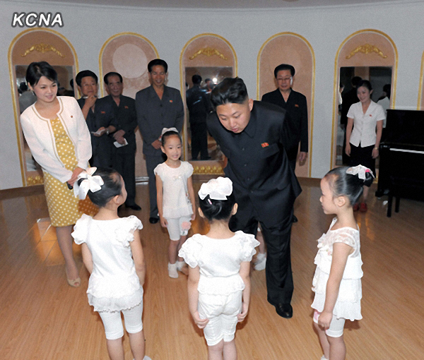 North Korea’s leader Kim Jong-un and an unidentified woman in a yellow dress talk to children during his recent visit to a kindergarten in Pyongyang. The scene was released by the Korean Central Television on Sunday. (Yonhap News)