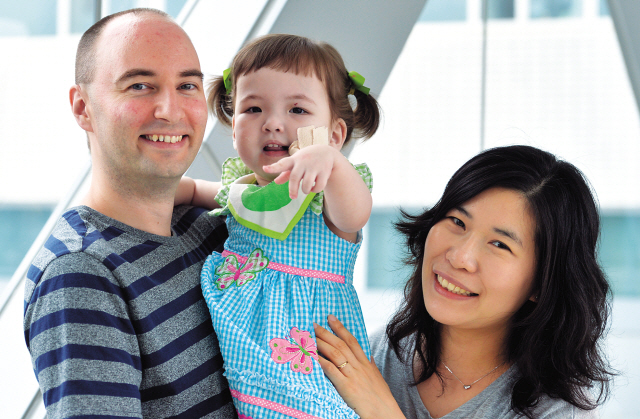 Hannah Warren (center), who was born without a windpipe, and her parents smile for the camera. The artificial windpipe, which is attached to Hannah’s face with bandages, is connected to her esophagus. (Kim Myung-sub/The Korea Herald)
