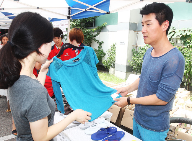 Lee Hyun-woo (right) tries to sell a shirt to a woman at the Social Welfare Society bazaar held in Yeoksam-dong, Seoul, on Wednesday. (Yonhap News)