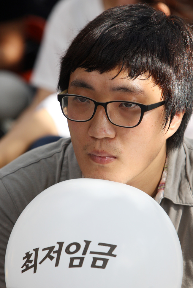 A young man holds a balloon with “minimum wage” written on it in a rally in front of the National Assembly in Yeouido, Seoul, on Tuesday, demanding an increase in this year’s minimum wage. ( Yonhap News)