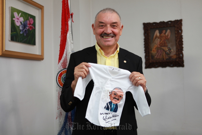 Paraguayan Ambassador Ceferino Valdez holds up clothes which will go to infants in need after the Benet Chogori Campaign named him an honorary ambassador in Seoul on Wednesday. (Korea Sarangbat Society)