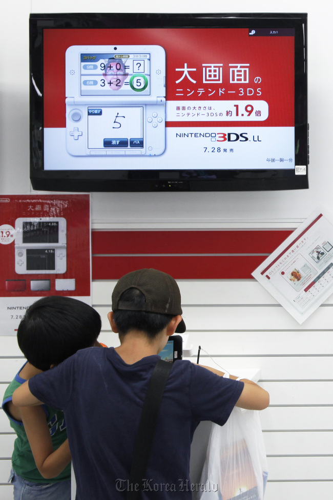 Boys try out Nintendo Co.’s 3DS LL handheld game console at a Yamada Denki Co. electronics store in Tokyo on Saturday. (Bloomberg)