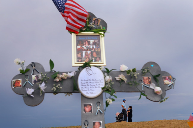 People are seen near a cross adorned with photographs of victims of the mass shooting at the Century 16 movie theater 30 in Aurora, Colorado on July. (AFP-Yonhap News)