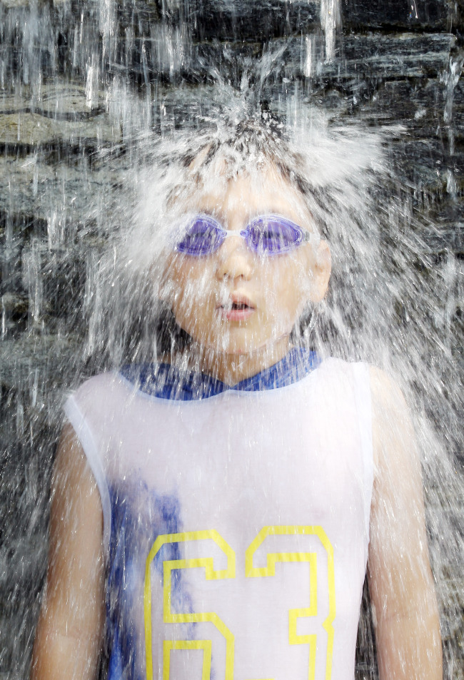 A child cools off under the waterfall at a swimming pool in Seoul Wednesday. Earlier in the day, the state weather agency issued a heat wave warning for Seoul.(Yonhap News)