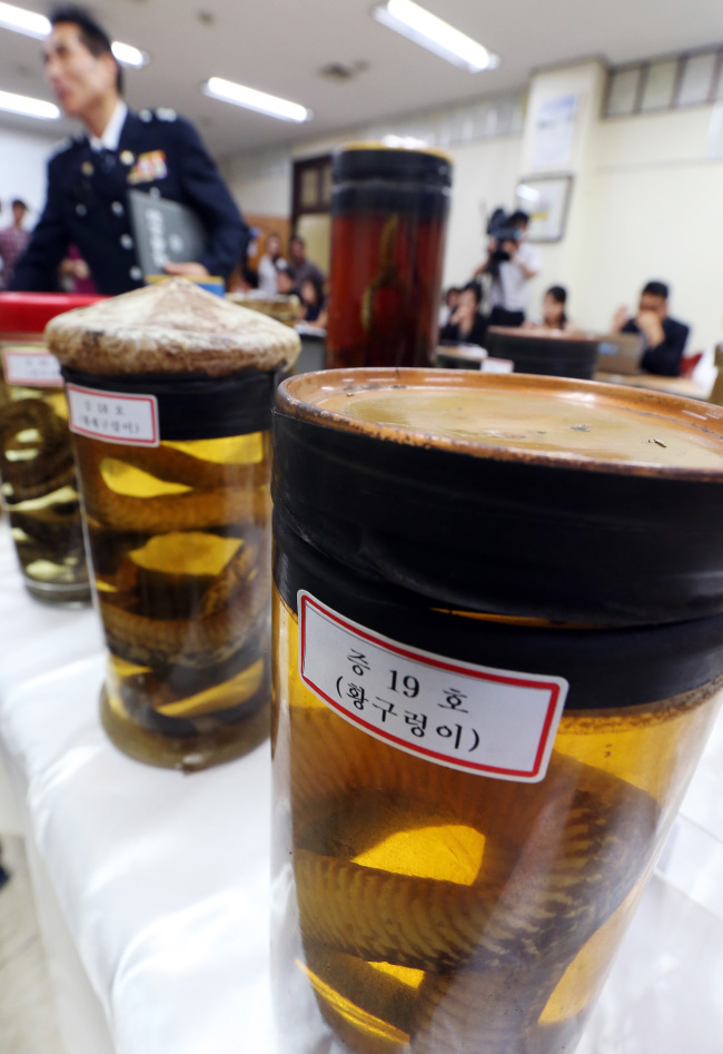 A police officer points at alcoholic beverages containing endangered snakes confiscated from a traditional health-supplement shop in Sinwol-dong in southwestern Seoul on Thursday. (Yonhap News)