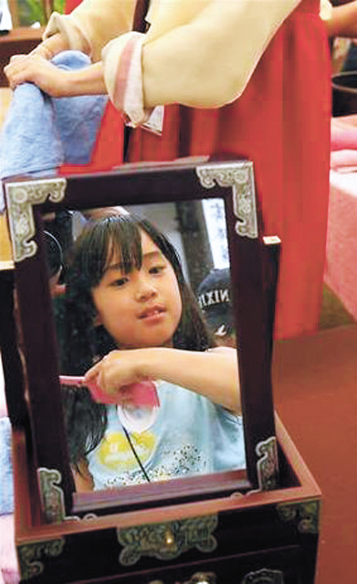 girl combs her hair while looking into a mirror used by women of earlier ages at a local cultural festival. (Yonhap News)