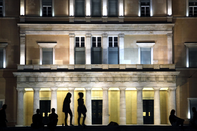 Pedestrians stand in front of the illuminated facade of the Greek parliament building in Athens. (Bloomberg)