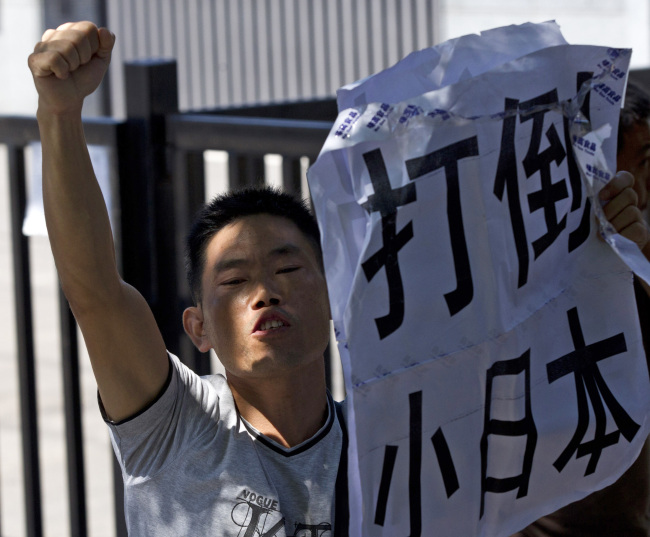 An anti-Japan protester shouts slogans while holding a poster, which reads 