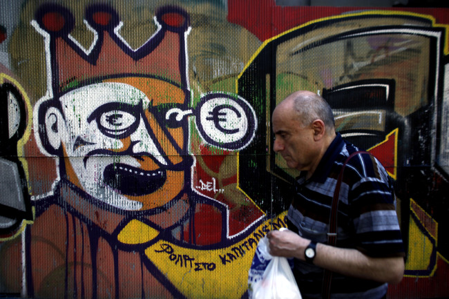 A pedestrian walks past euro-crisis graffiti painted on a wall in Athens. (Bloomberg)