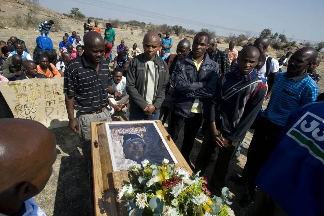 Mineworkers pray on Friday over the coffin containing the body of Mpuzeni Ngxande, one of the 34 striking miners that were killed by police on Aug. 16, in front of the rocky outcrop where the men were shot, an informal settlement near the Lonmin mine in Marikana, South Africa. (AFP-Yonhap News)