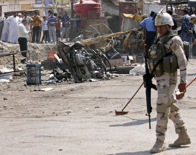 An Iraqi soldier stands guard as security forces inspect the scene of a car bomb attack in Basra, Iraq, Sunday. (AP-Yonhap News)