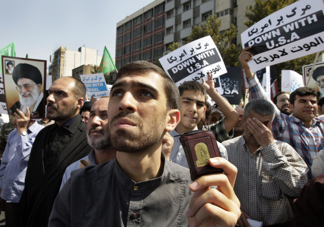 An Iranian worshipper holds a copy of the Quran, Muslims’ holy book, as the others hold up anti-U.S. and anti-Israel placards and posters showing Iranian supreme leader Ayatollah Ali Khamenei, and late revolutionary founder Ayatollah Khomeini, during a protest after their Friday prayers, as part of widespread anger across the Muslim world about a film ridiculing Islam’s Prophet Muhammad. (AP-Yonhap News)