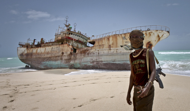 In this photo taken Sunday, masked Somali pirate Abdi Ali stands near a Taiwanese fishing vessel that washed up on shore after the pirates were paid a ransom and released the crew, in the once-bustling pirate den of Hobyo, Somalia. (AP-Yonhap News)