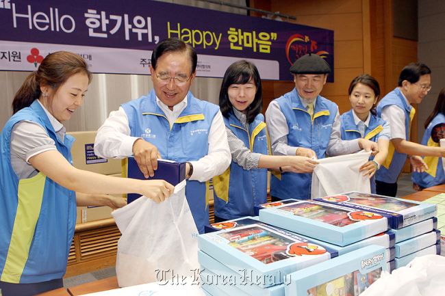 Shinhan Financial Group chairman Han Dong-woo (second from left) helps pack gift sets to be delivered to poor children across the nation at the lender’s headquarters last week. (Shinhan Financial Group)